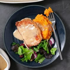 a blue plate topped with meat covered in gravy next to a bowl of mashed potatoes