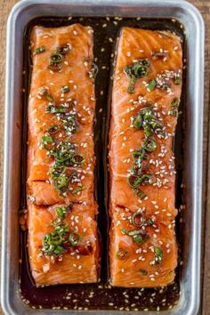 two salmon fillets in a baking pan with sesame seeds and seasoning on top