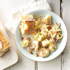 a white plate topped with pasta next to a piece of bread on top of a wooden table