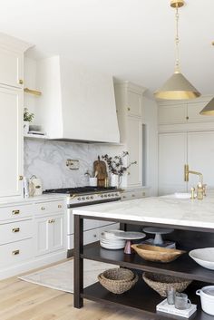 a kitchen with white cabinets and marble counter tops, gold accents on the hoods