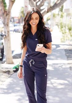 a woman in scrubs is walking down the street and looking at her cell phone