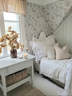 a white bed sitting under a window next to a table with a vase on it