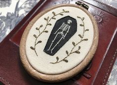 an embroidered brooch with a skeleton holding a knife in it's hand on top of a leather case