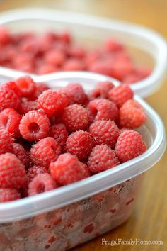 raspberries in plastic containers sitting on a wooden table next to another container full of raspberries