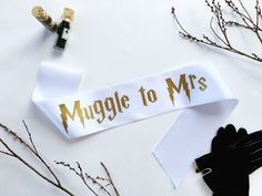 a white ribbon with gold lettering on it next to black gloves and twig sprouts