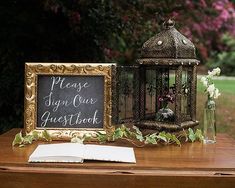 a wooden table topped with a sign next to a birdcage filled with flowers