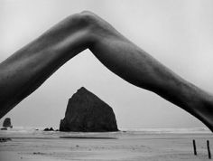 a black and white photo of a person's legs on the beach with rocks in the background