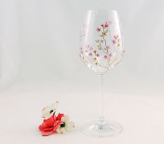 a wine glass with flowers painted on it next to a small flower stemer,