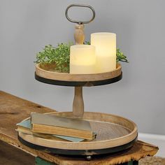 two candles sitting on top of a wooden tray with books and plants in it next to a candle holder