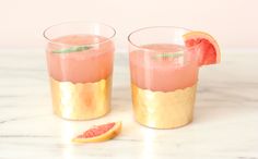 two glasses filled with watermelon and gold rimmed drinks on a marble table