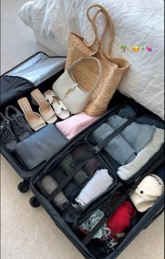 an open suitcase on the floor with shoes and handbags in it's compartment