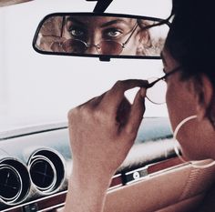 a woman is looking in the rear view mirror as she brushes her teeth with glasses