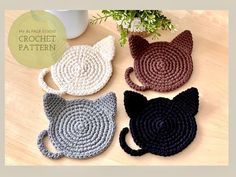 four crocheted cat coasters sitting on a table next to a potted plant