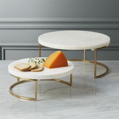 two tables with cheese and bread on them in front of a gray wall or floor