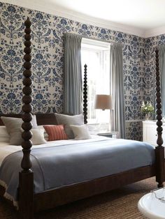 a bedroom with blue and white wallpaper and four poster bed in front of a window