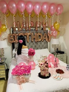 a woman sitting on top of a bed next to pink and gold balloons