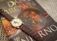 a watch sitting on top of a book next to a brown leather strap and cover