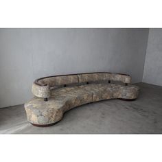 a curved couch sitting on top of a cement floor next to a wall with no one in it