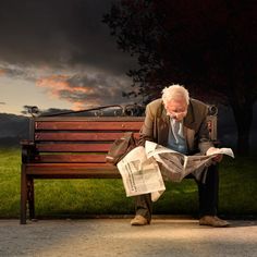 an old man sitting on a bench reading a newspaper