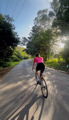 a person riding a bike down a road in the sun with trees and grass behind them