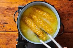 corn being cooked in a pot on the stove with tongs and water next to it