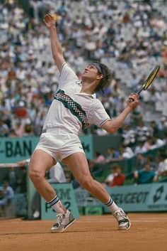 a man holding a tennis racquet on top of a tennis court in front of a crowd