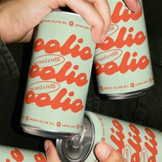 two cans of pale green and orange soda being held by someone's left hand