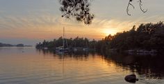 the sun is setting over some water with boats in it and trees on either side