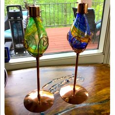 two colorful glass vases sitting on top of a wooden table next to a window