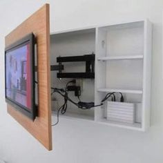 a tv mounted to the side of a white wall next to a shelf with wires