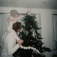 a woman holding a baby up to a christmas tree