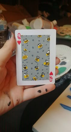 a person holding up a playing card with bees on it's back and hearts in the middle