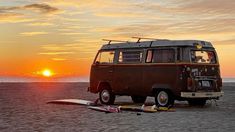 an old van is parked on the beach with surfboards in front of it as the sun sets