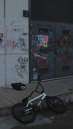 a bicycle parked on the sidewalk next to a building with graffiti all over it