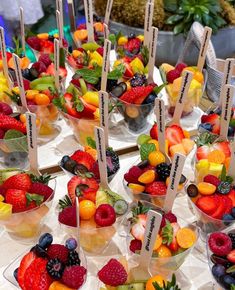 a table topped with lots of different types of fruit in cups filled with ice cream