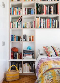 a white bookcase filled with books next to a bed and a basket on the floor