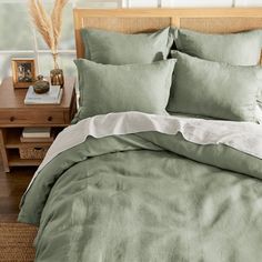 a bed with green sheets and pillows on top of a wooden headboard next to a night stand