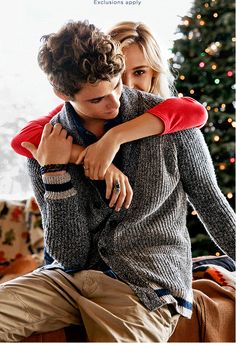 a young man and woman embracing each other in front of a christmas tree with lights