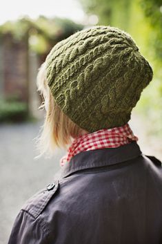 a young child wearing a green knitted hat and neck tie looking at the street