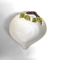 a white heart shaped bowl with two green leaves on the top and brown beads in the middle