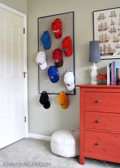 several hats are hanging on a pegboard in the corner of a room next to a dresser