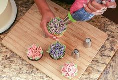 someone is decorating cupcakes on a cutting board