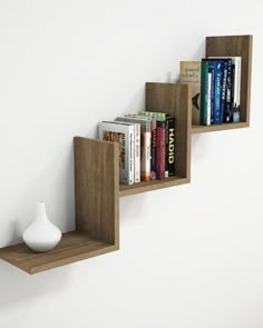 three wooden shelves with books on them against a white wall, one has a vase and the other holds several books