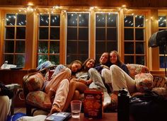 three women sitting on a couch in front of two windows with lights strung from them