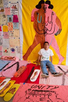 a man sitting on top of a bed covered in pink and yellow sheets next to skateboards