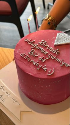 a pink birthday cake with white frosting and writing on the top is sitting on a table