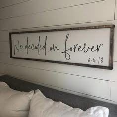 a wooden sign that says we decided on forever above a bed with white sheets and pillows