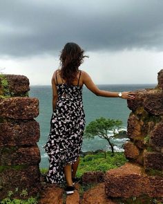 a woman standing on top of a stone wall next to the ocean