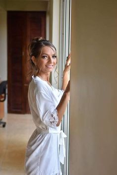 a woman in a white robe leaning against a wall with her hand on the door handle