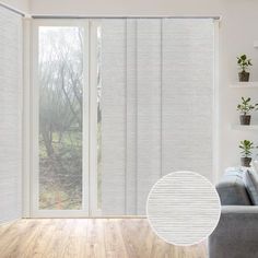 a living room with white walls and wooden floors, two windows covered in vertical blinds